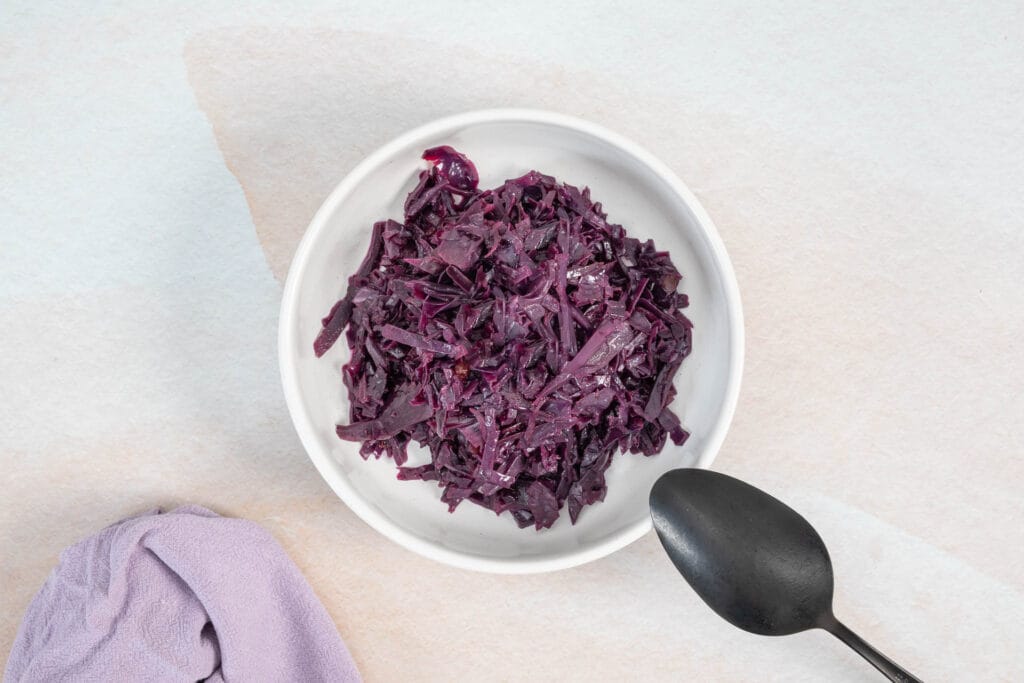 Veganes Rotkraut in einer weissen Schale, angerichtet als klassische Beilage, mit Löffel im Bild