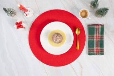 Veganes Weihnachtsdessert: Bratapfel auf cremiger Vanillesauce, angerichtet mit Kerze und Mini-Tannen.