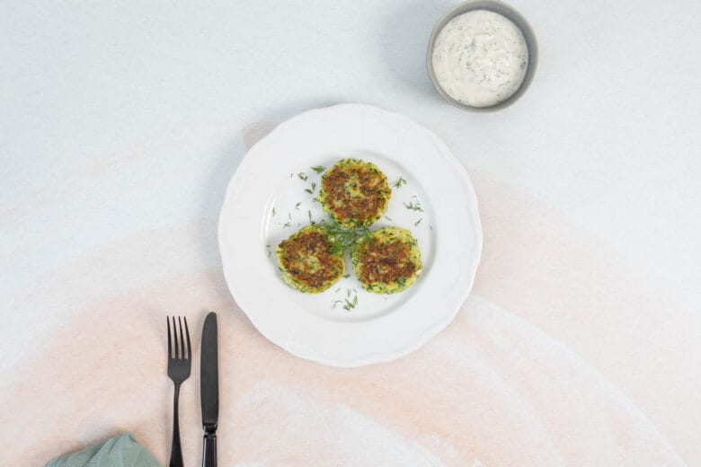 Knusprige vegane Zucchetti-Puffer mit frischem Joghurt-Dip angerichtet als einfaches Hauptgericht