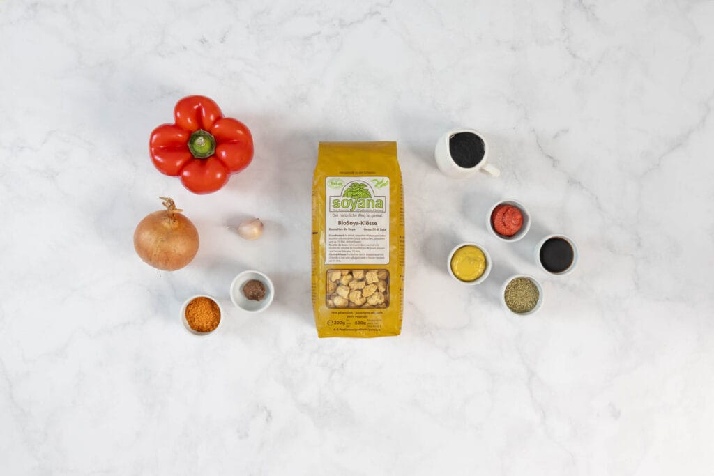 Zutaten für veganes Gulasch Rezept mit Sojaschnetzeln, Paprika, Zwiebeln und Gewürzen auf der Arbeitsfläche