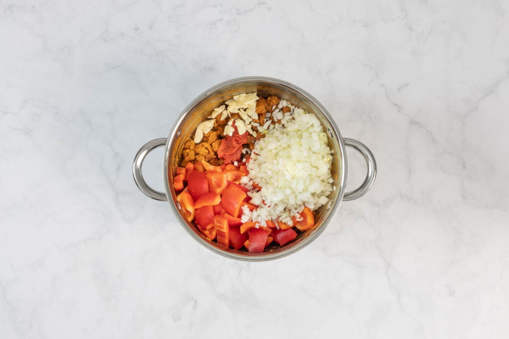 Paprika, Zwiebeln und Knoblauch werden zum veganen Gulasch im Topf gegeben