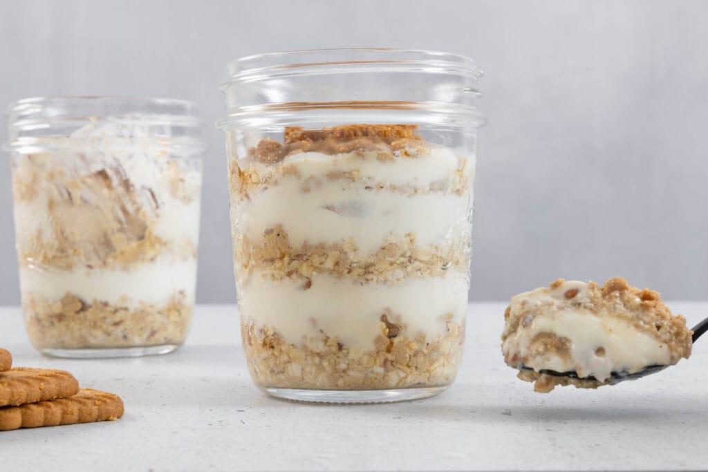 Cremige vegane Overnight Oats Japanese Cheesecake mit Löffel und Lotus Biscoff Biscuits im Glas
