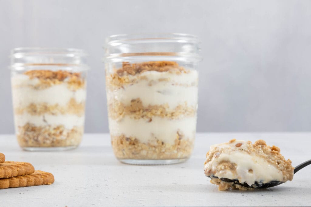 Cremige vegane Japanese Cheesecake Overnight Oats im Einmachglas mit Löffel und Lotus Biscoff Biscuits