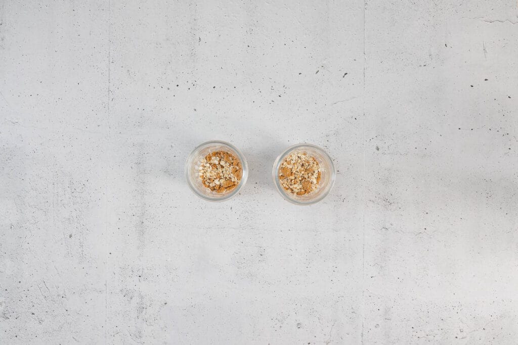 Erste Schicht der Hafer-Biscoff-Mischung in zwei Einmachgläsern für vegane Overnight Oats Japanese Cheesecake