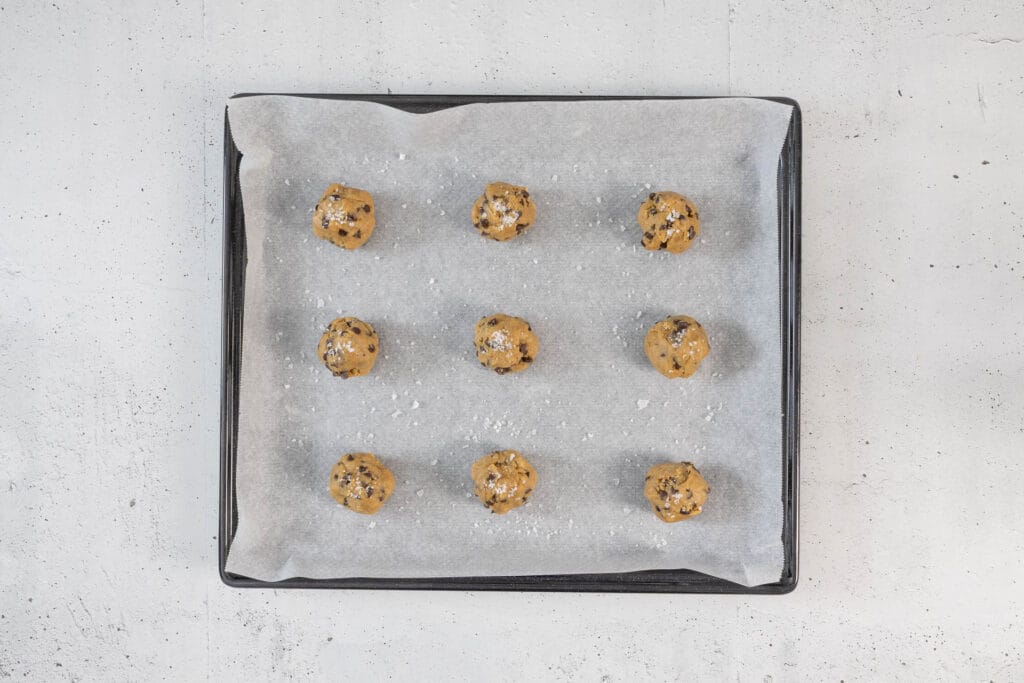 Cookie-Teigkugeln mit Meersalz auf dem Backblech – ungepresst, da sie beim Backen von selbst flach werden