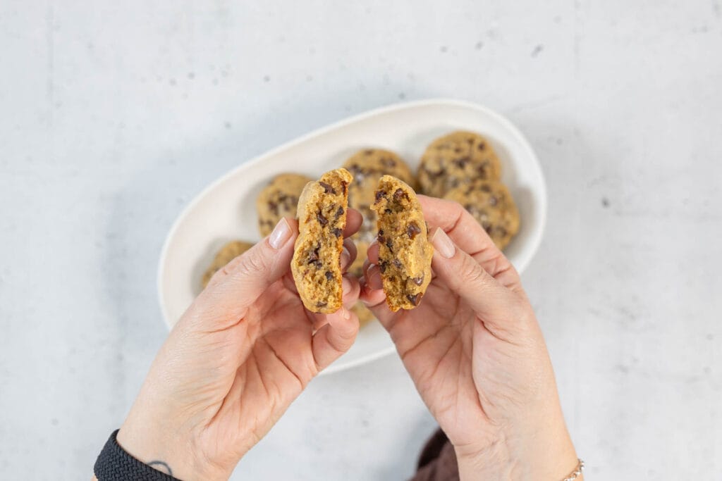 Zwei Hände brechen einen Chocolate Chip Cookie auf – die chewy, saftige Innentextur zeigt den Unterschied zum gewöhnlichen Keks