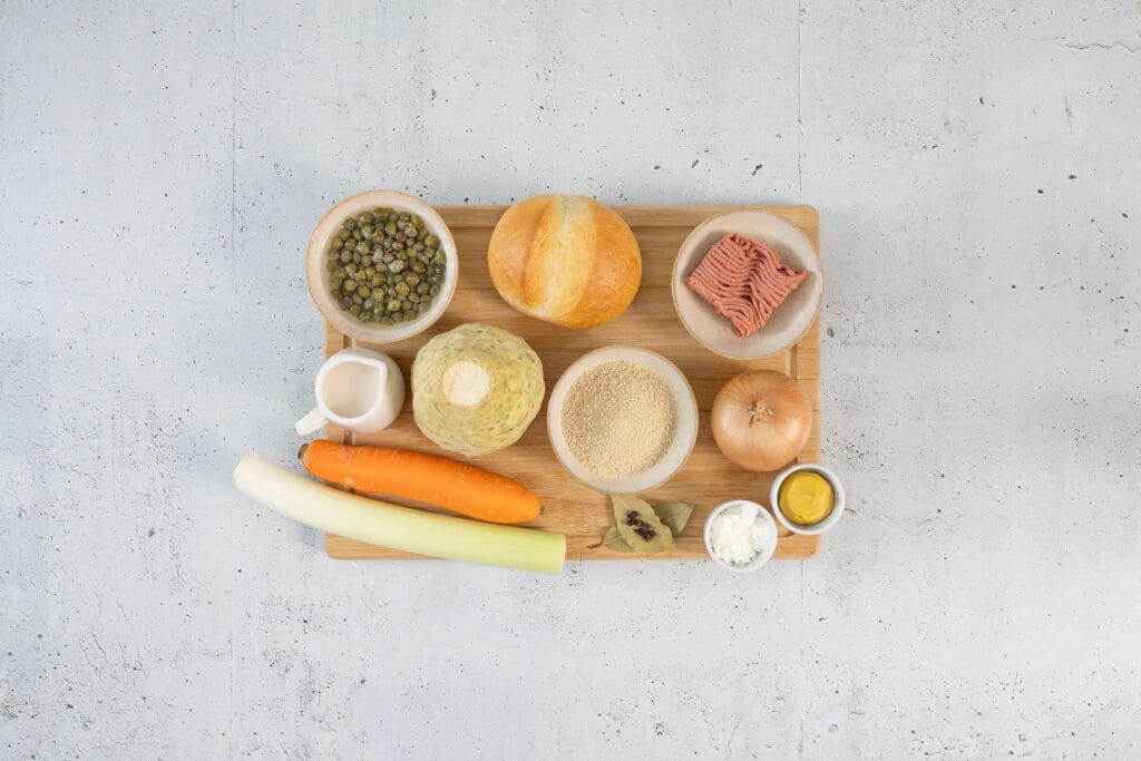 Zutaten für vegane Königsberger Klopse auf Holzbrett: veganes Hack, Brötchen, Kapern, Sellerie, Karotte und Lauch