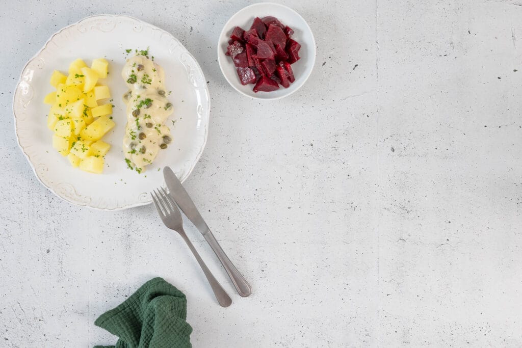 Vegane Königsberger Klopse mit Kapernsauce, Salzkartoffeln und Randensalat – Aufsicht mit Besteck