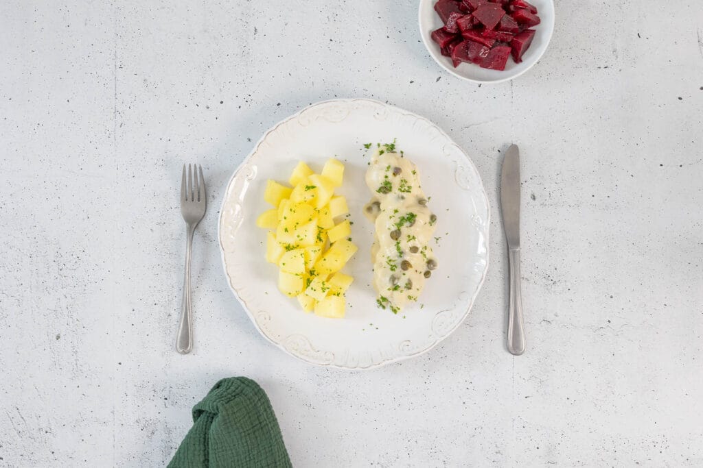 Nahaufnahme der veganen Königsberger Klopse mit Kapernsauce und Petersilie auf Salzkartoffeln