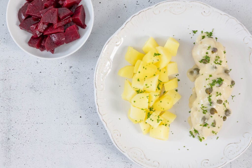 Portion vegane Königsberger Klopse mit Kapernsauce, serviert mit Salzkartoffeln und einer Schale Rote Bete