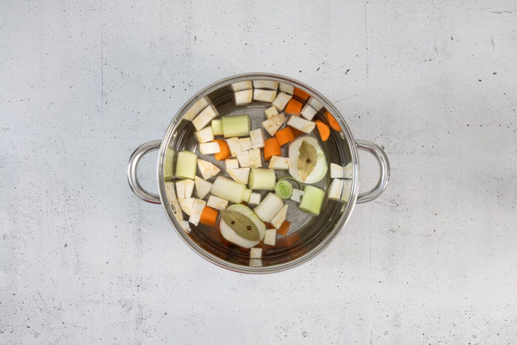 Klopsbrühe mit Lauch, Karotte, Sellerie und Zwiebel im grossen Topf beim Aufkochen