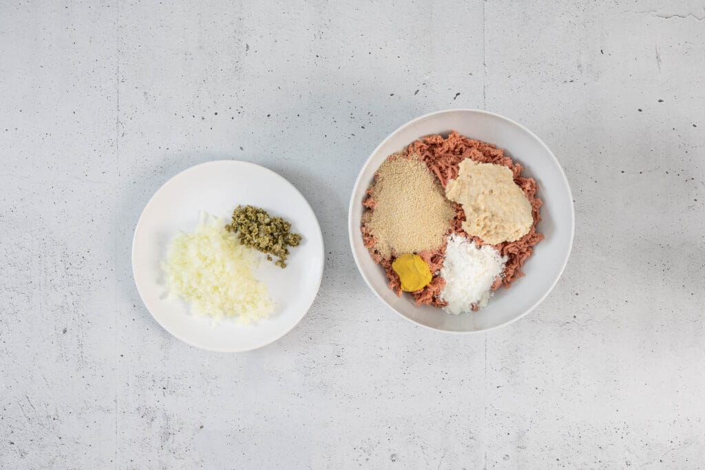 Zutaten für die vegane Klopsmasse: veganes Hack mit Paniermehl, Senf, Maisstärke sowie gehackte Zwiebel und Kapern