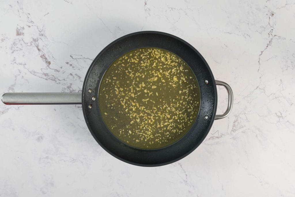 Mit Weisswein und Gemüse-Bouillon abgelöschte Knoblauchsauce in der Pfanne, kurz vor dem Einkochen für die Linguine mit Pilz-Muscheln