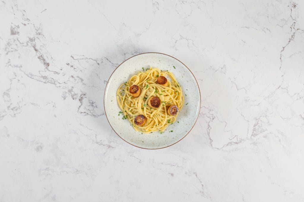 Linguine mit veganen Pilz-Muscheln aus Kräuterseitlingen serviert auf einem rustikalen Teller, garniert mit gehackter Petersilie
