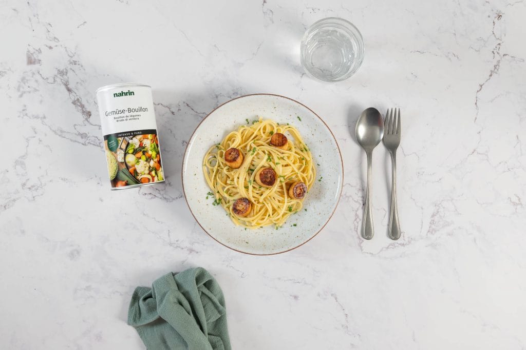 Servierfertige Linguine mit Pilz-Muscheln in Weissweinsauce mit Gemüse-Bouillon von Nahrin, Wasserglas und Besteck