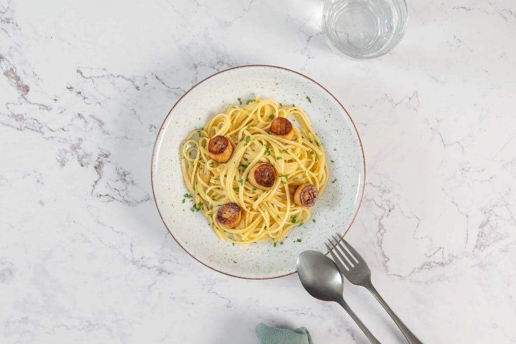 Vegane Muschelpasta von oben mit Linguine, Kräuterseitling-Jakobsmuscheln und Petersilie auf einem rustikalen Teller
