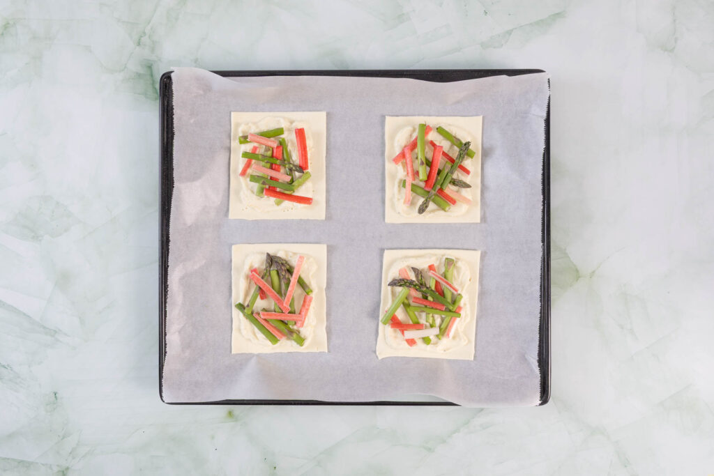 Mit grünem Spargel und Rhabarber belegte Blätterteig-Tartelettes vor dem Backen