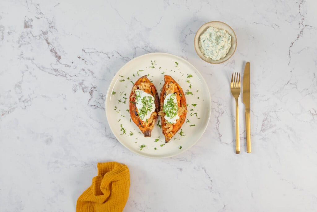 Angerichtete vegane Loaded Sweet Potatoes mit Kräuterdip, Goldbesteck und Serviette