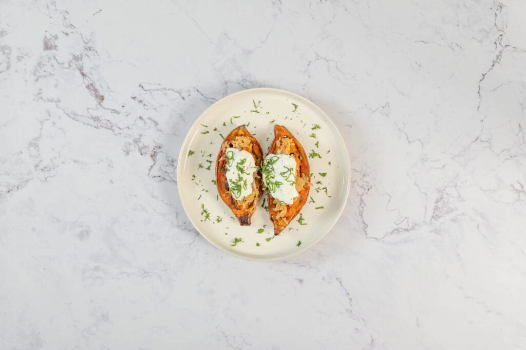 Servierfertige vegane gefüllte Süsskartoffeln mit Sauerrahm und Frühlingszwiebeln von oben