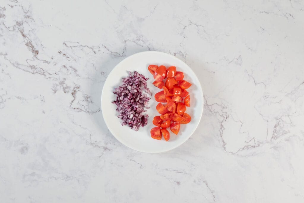 Fein gehackte rote Zwiebel und geviertelte Cherrytomaten für die proteinreiche Bohnenfüllung