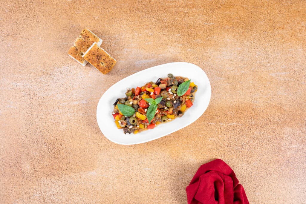 Vegane sizilianische Caponata mit Oliven, Peperoni und Pinienkernen, serviert mit frischem Focaccia