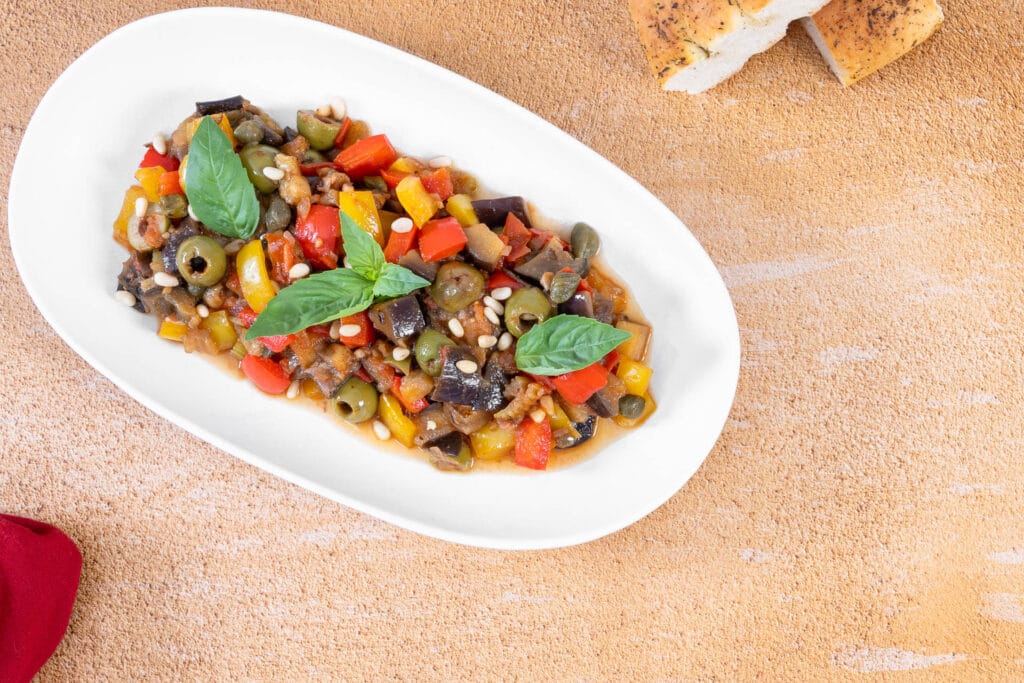 Nahaufnahme der Caponata mit glänzendem Agrodolce, grünen Oliven, Peperoni und Pinienkernen