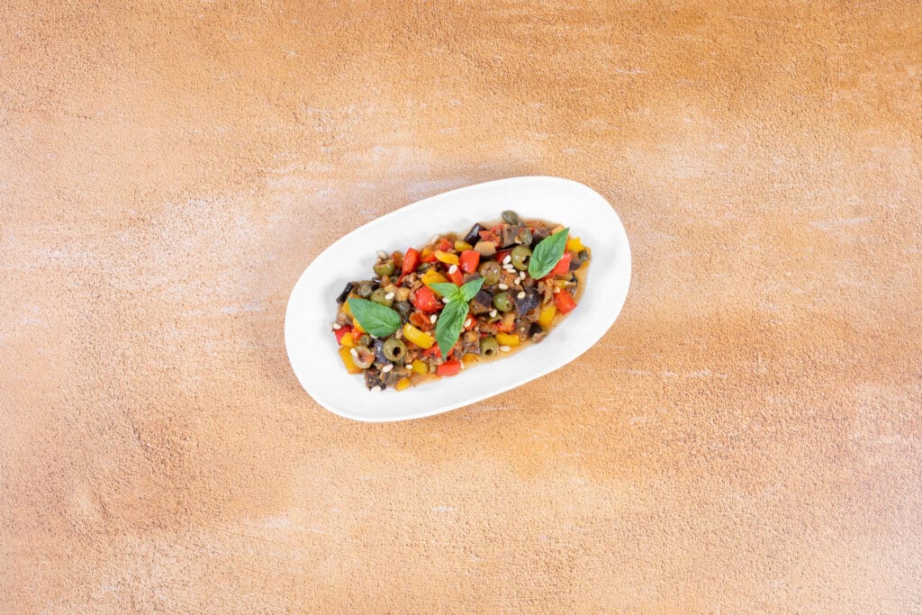 Kleine Portion vegane Caponata als Antipasto, garniert mit Basilikum und Pinienkernen