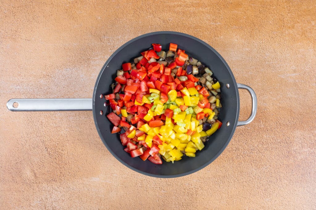 Tomaten, rote und gelbe Peperoni und Sellerie kommen zu den Auberginen in die Pfanne