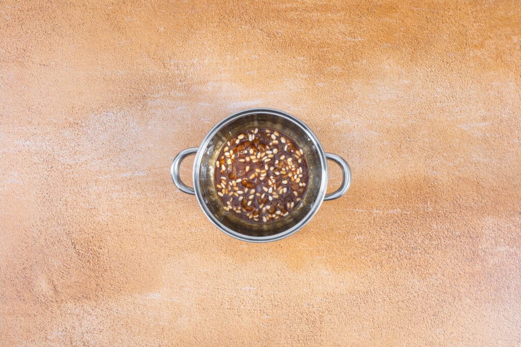Fertige süss-saure Agrodolce-Sauce mit Pinienkernen und Rosinen in einer kleinen Pfanne