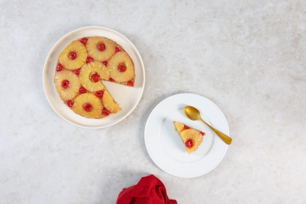 Angeschnittener veganer Ananaskuchen mit einem Stück auf separatem Teller und goldenem Löffel