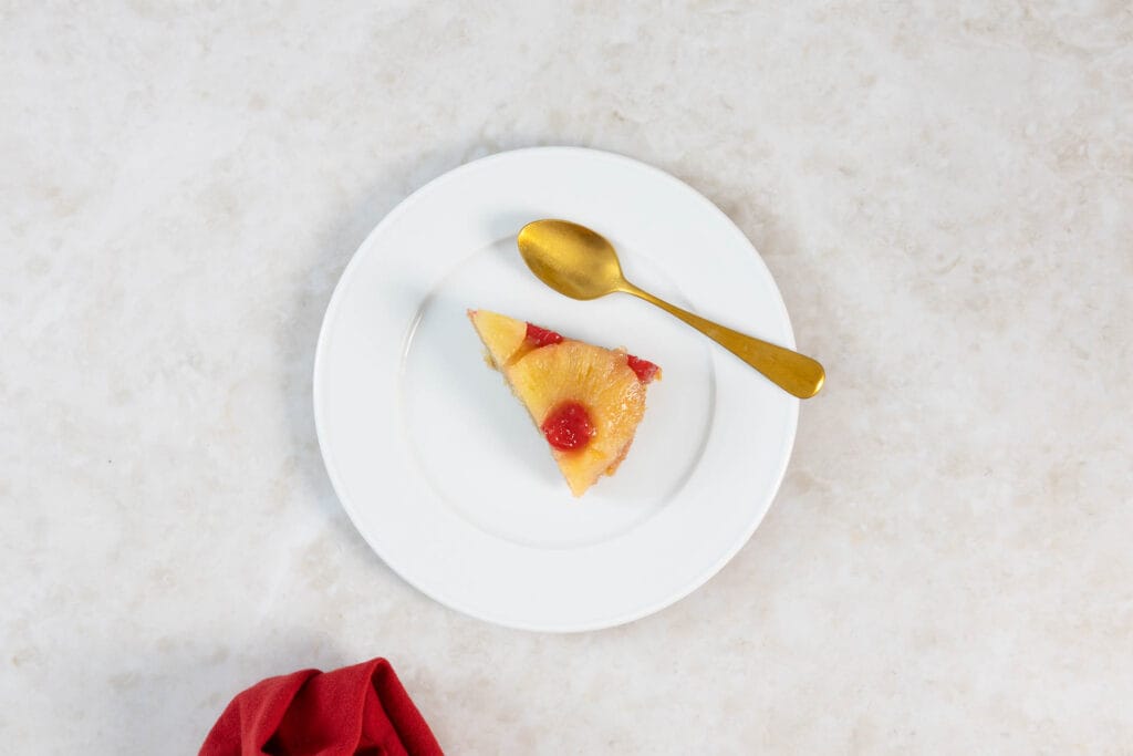 Einzelnes Stück gestürzter Ananaskuchen mit Ananas und Cocktailkirsche auf weissem Teller