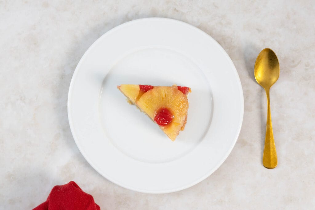 Tortenstück des veganen Ananaskuchens von oben mit goldenem Löffel und roter Serviette
