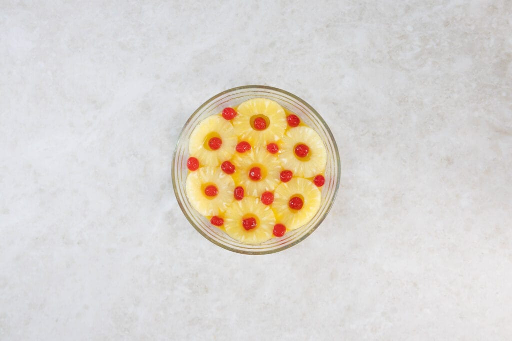 Veganer Ananas Upside Down Cake vor dem Backen: Ananasringe mit Cocktailkirschen in der Form geschichtet