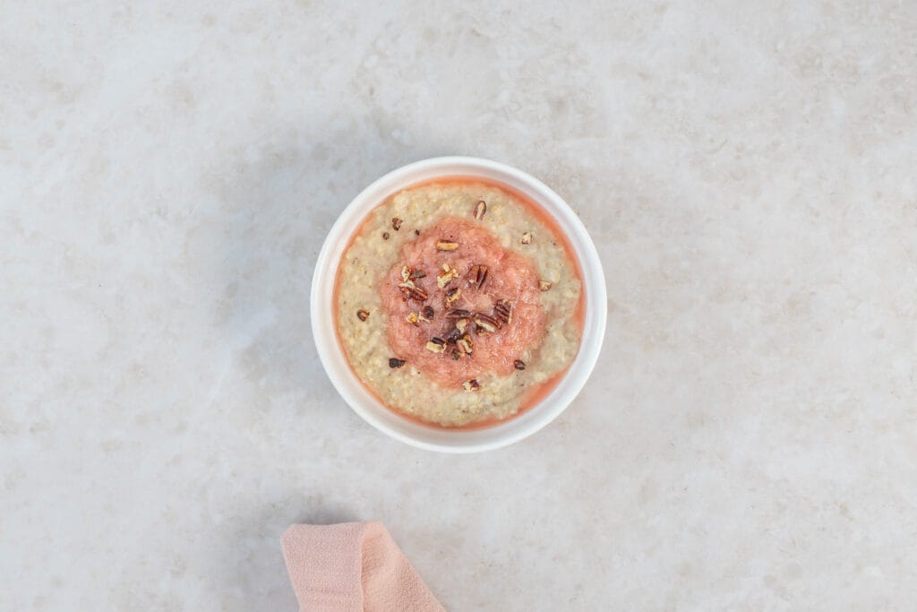 Cremiges Porridge mit süss-saurem Rhabarberkompott und Nüssen in weisser Schale, mit rosa Serviette
