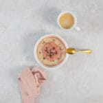 Rhabarber-Porridge mit goldenem Löffel, Kaffeetasse und rosa Tuch als frühlingshaftes Frühstücksgedeck