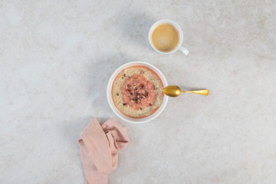 Rhabarber-Porridge mit goldenem Löffel, Kaffeetasse und rosa Tuch als frühlingshaftes Frühstücksgedeck