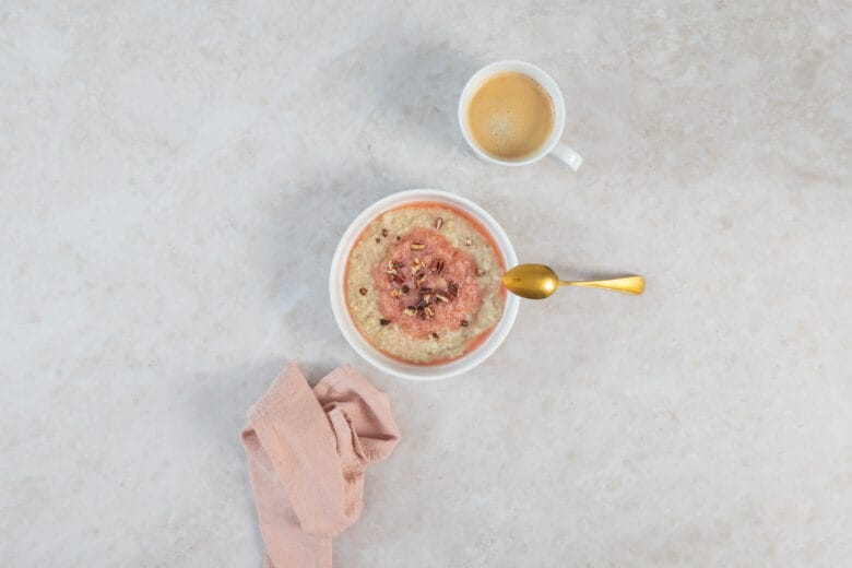 Rhabarber-Porridge mit goldenem Löffel, Kaffeetasse und rosa Tuch als frühlingshaftes Frühstücksgedeck