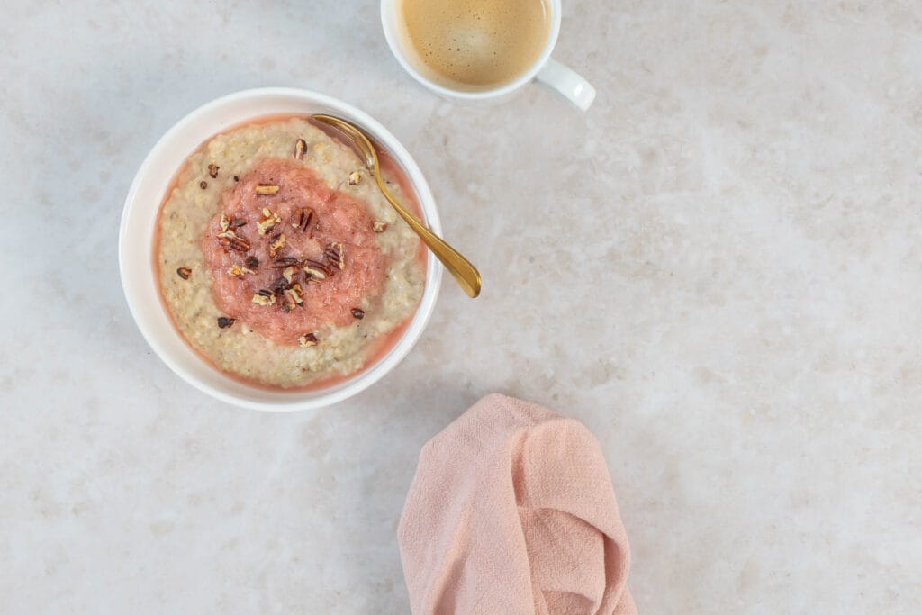 Cremiges Rhabarber-Porridge mit Nüssen und goldenem Löffel, daneben Kaffee und Serviette