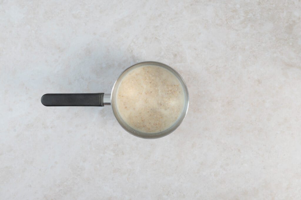 Geröstete Haferflocken köcheln mit Wasser und Sojamilch im Topf zu cremigem veganem Porridge