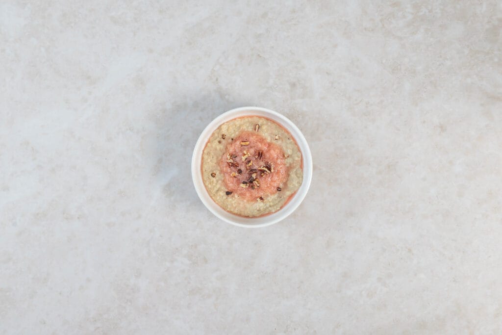 Veganes Porridge mit Rhabarberkompott und Nüssen in einer kleinen Schale von oben