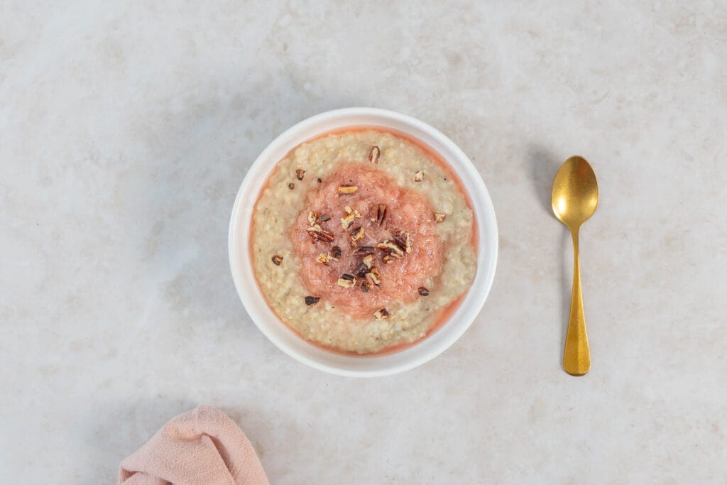 Schale veganes Porridge mit Rhabarberkompott und gerösteten Pekannüssen, daneben ein goldener Löffel