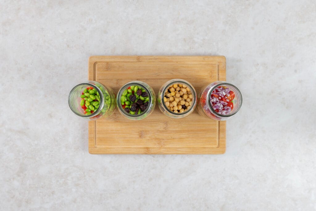 Vier Gläser beim Schichten mit Edamame, Cranberries, Kichererbsen und roten Zwiebeln