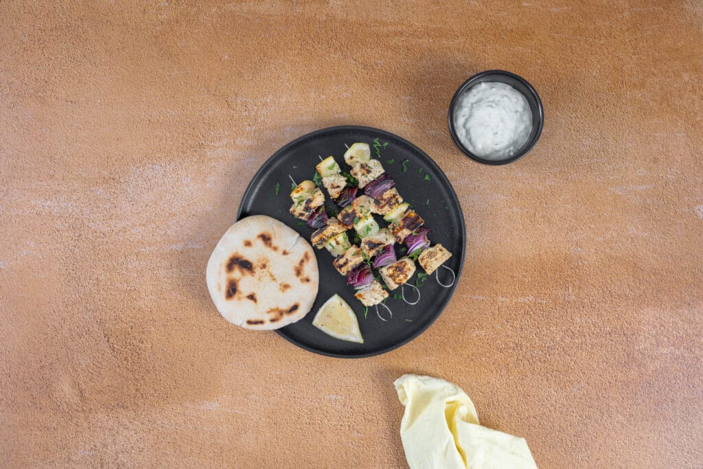 Griechische Tofu Souvlaki Spiesse mit Tzatziki und Pita auf einem schwarzen Teller