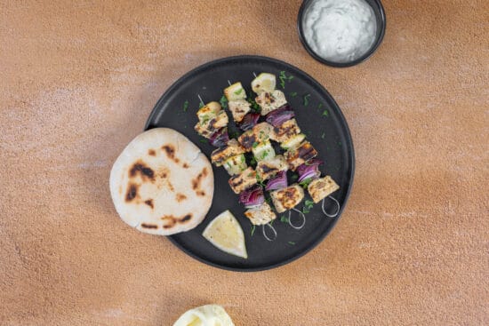 Vegane Tofu Souvlaki Spiesse mit roter Zwiebel und Zitrone, serviert mit Tzatziki und Pitabrot