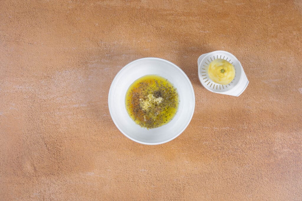Marinade für Tofu Souvlaki aus Olivenöl, Zitronensaft, Oregano und Knoblauch neben einer ausgepressten Zitrone