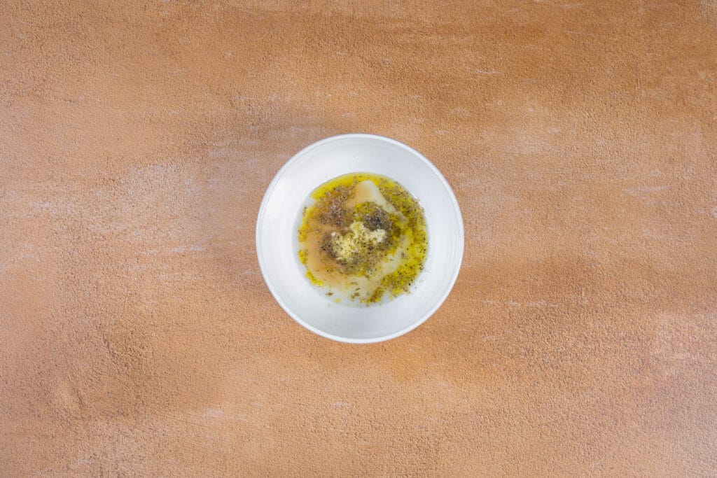 Griechische Souvlaki Marinade mit Oregano, Zitrone und Knoblauch in einer weissen Schüssel verrührt