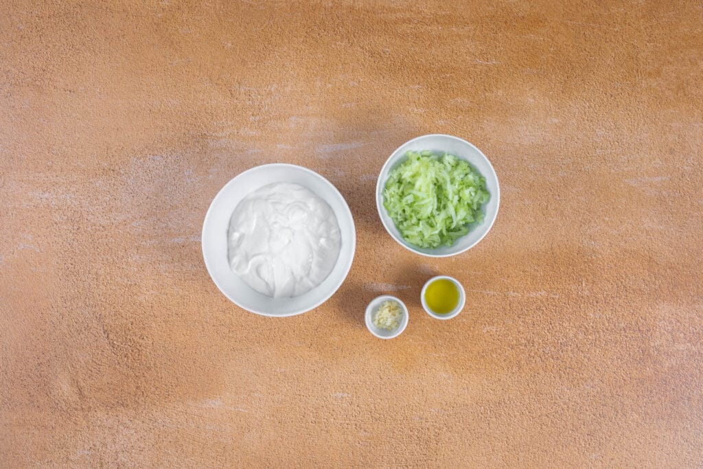 Zutaten für veganes Tzatziki: abgetropfter Joghurt, geraffelte Gurke, Knoblauch und Olivenöl