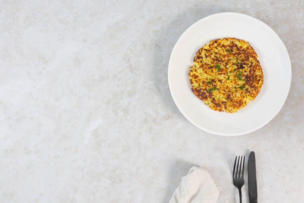 Schweizer Rösti vegan, goldbraun gebraten und mit frischer Petersilie garniert