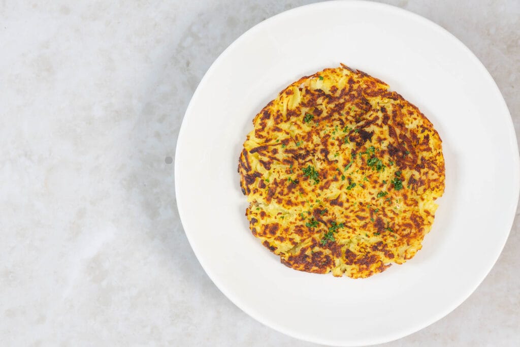 Goldbraune vegane Rösti mit knusprigem Rand, serviert auf weissem Teller