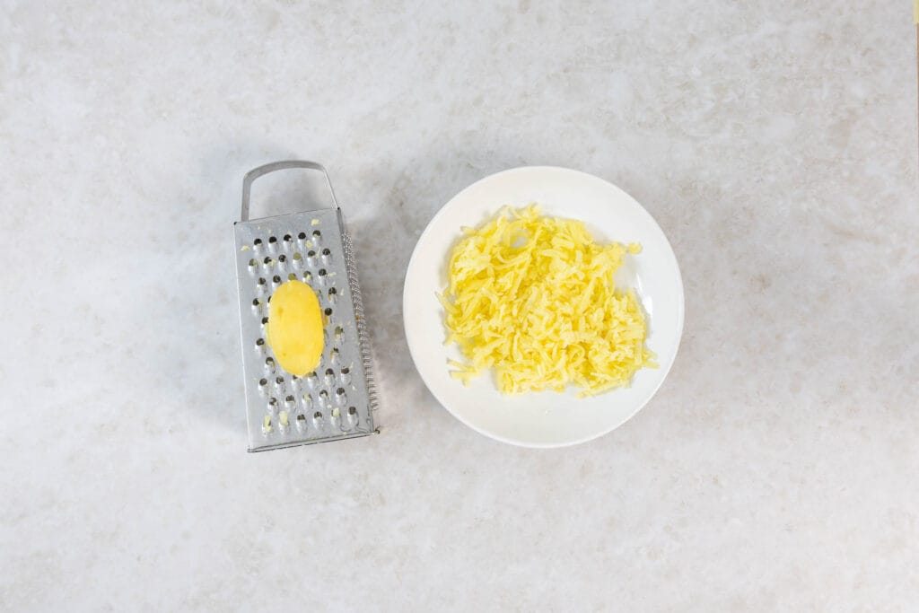 Gekochte Kartoffel wird mit der Röstiraffel für die vegane Rösti gerieben